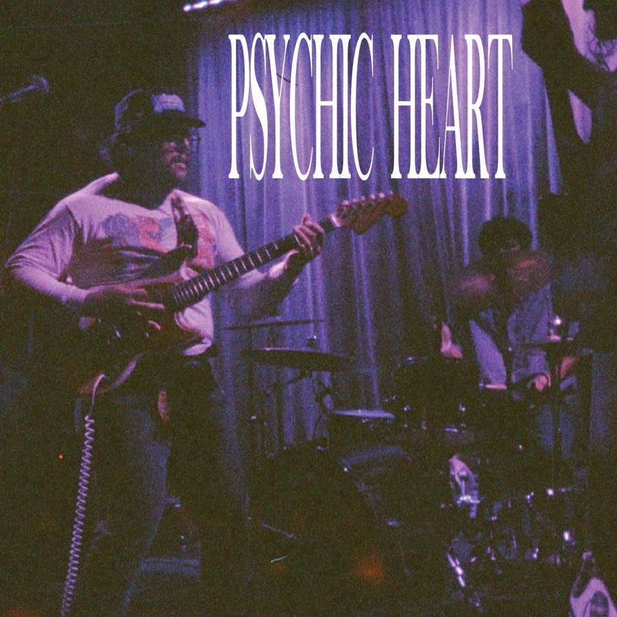 A purple-tinted photograph of the band playing live, with PSYCHIC HEART lettered across the top.